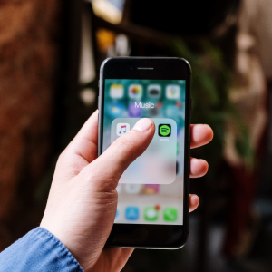 Image of a phone in a hand. The phone screen shows apple music and spotify