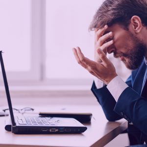 A photo of a man looking at his laptop with his head in his hand looking frustrated